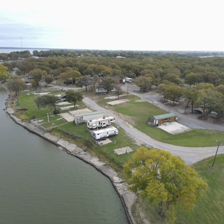 A scenic view of full hookup RV sites surrounded by lush trees, with Lake Tawakoni in the background, showcasing the peaceful lakeside atmosphere at 429 Resort & Marina in Quinlan, TX.